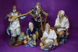 Five Chinese figurines of mean in various stances, one with instrument, another with an axe etc.
