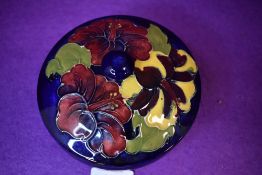 A lidded Moorcroft bowl having cobalt blue ground with hibiscus pattern to lid in reds, ochre and