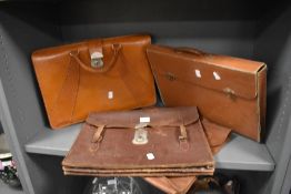 Three leather brief cases or satchels, and one similar cardboard example.