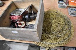 A wooden box containing mixed fishing tackle including reels,flies and a keep net.