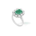 AN EMERALD AND DIAMOND CLUSTER RING The central cut-cornered rectangular emerald within a