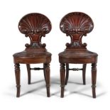 A PAIR OF REGENCY CARVED MAHOGANY HALL CHAIRS, with shell backs and solid seats, raised on turned