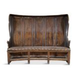 A GEORGE I OAK AND WALNUT TALL BACK SETTLE, the raised five panel back with side guards,