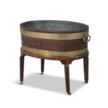 A GEORGE III MAHOGANY AND BRASS BOUND OVAL WINE COOLER with zinc lining and flanked by robust brass