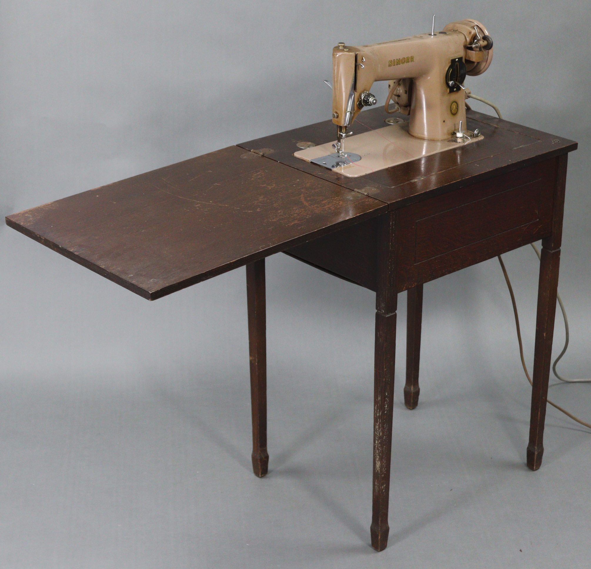 A Singer electric-operated sewing machine, w.o. in oak cabinet on four square tapered legs, “ wide.