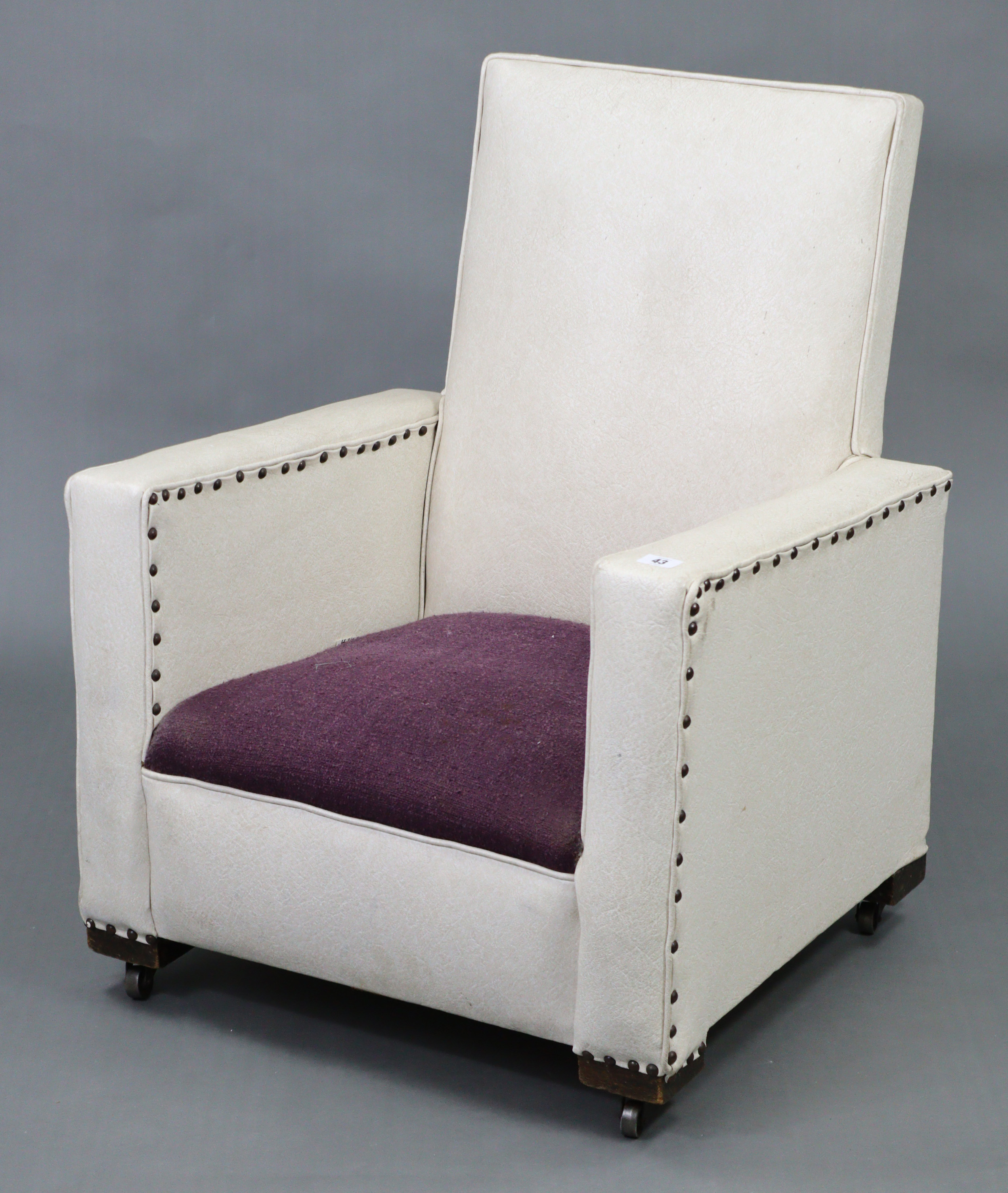 A mid-20th century square-back child’s easy chair upholstered cream rexine, & on castors.
