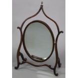 An early 19th century oval swing toilet glass in mahogany skeleton frame, with foliate terminal & on