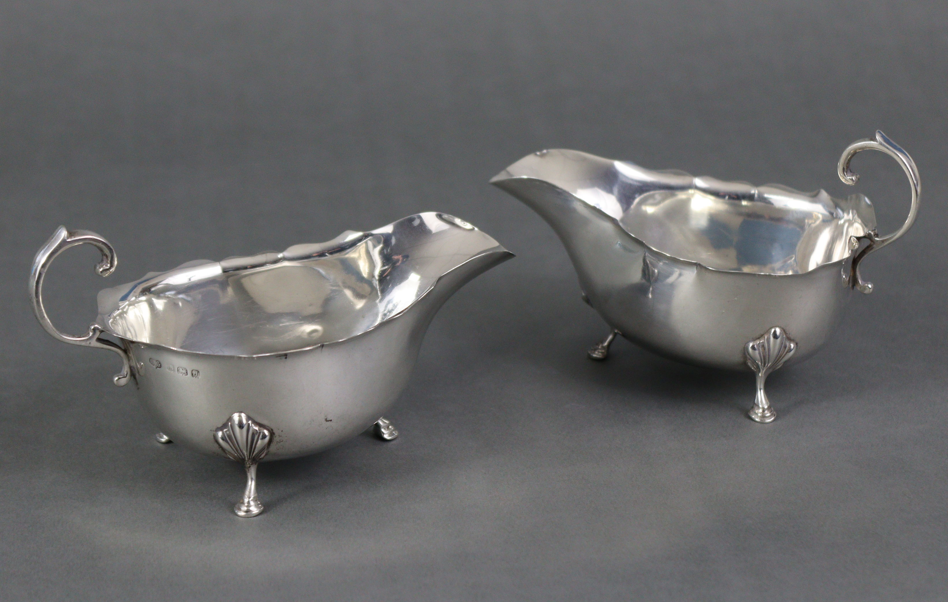 A pair of Georgian-style silver sauce boats, each with scroll handle & card-cut rims, on three shell