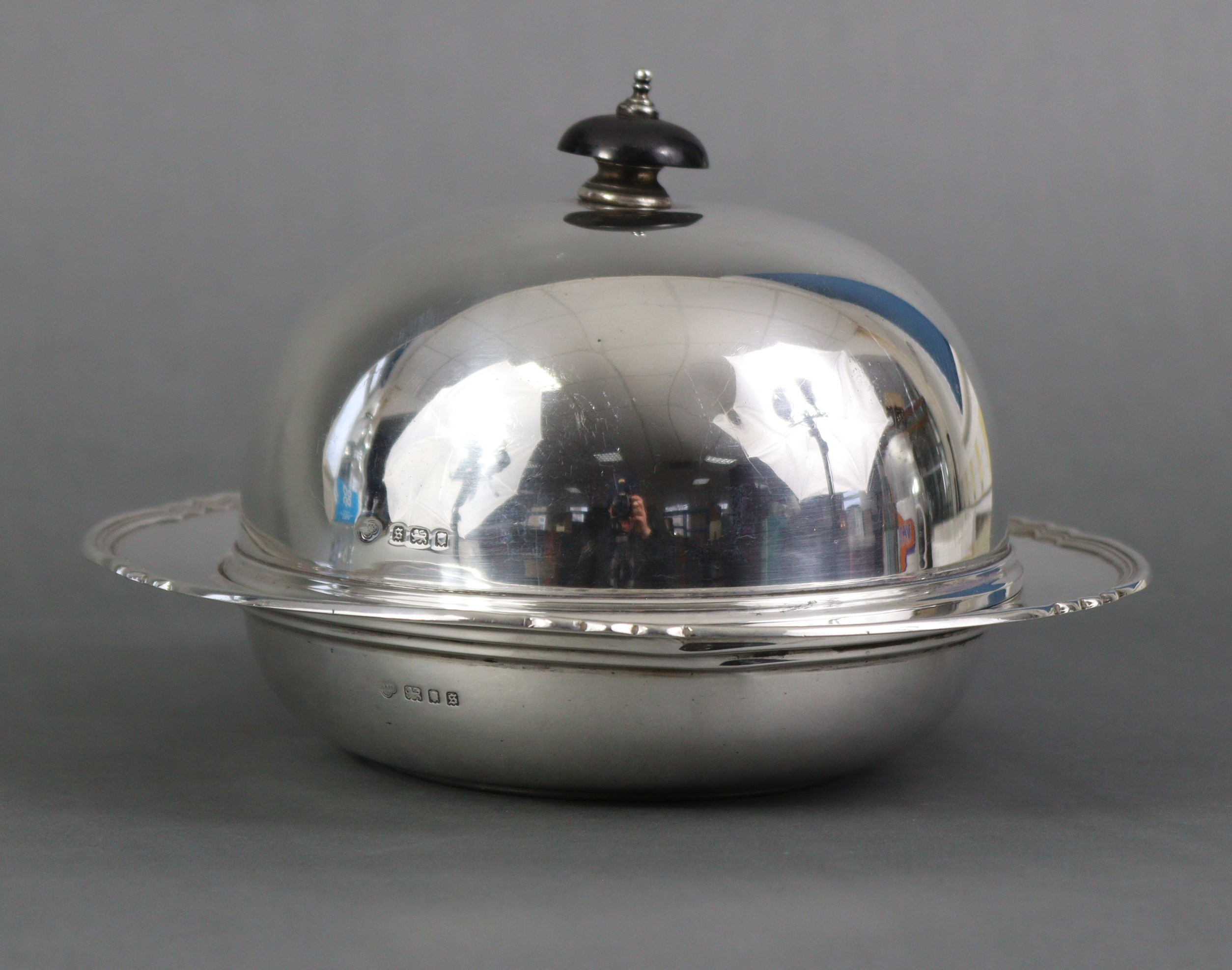 A silver circular muffin dish with ebonised finial to the domed lid, with shaped & reeded