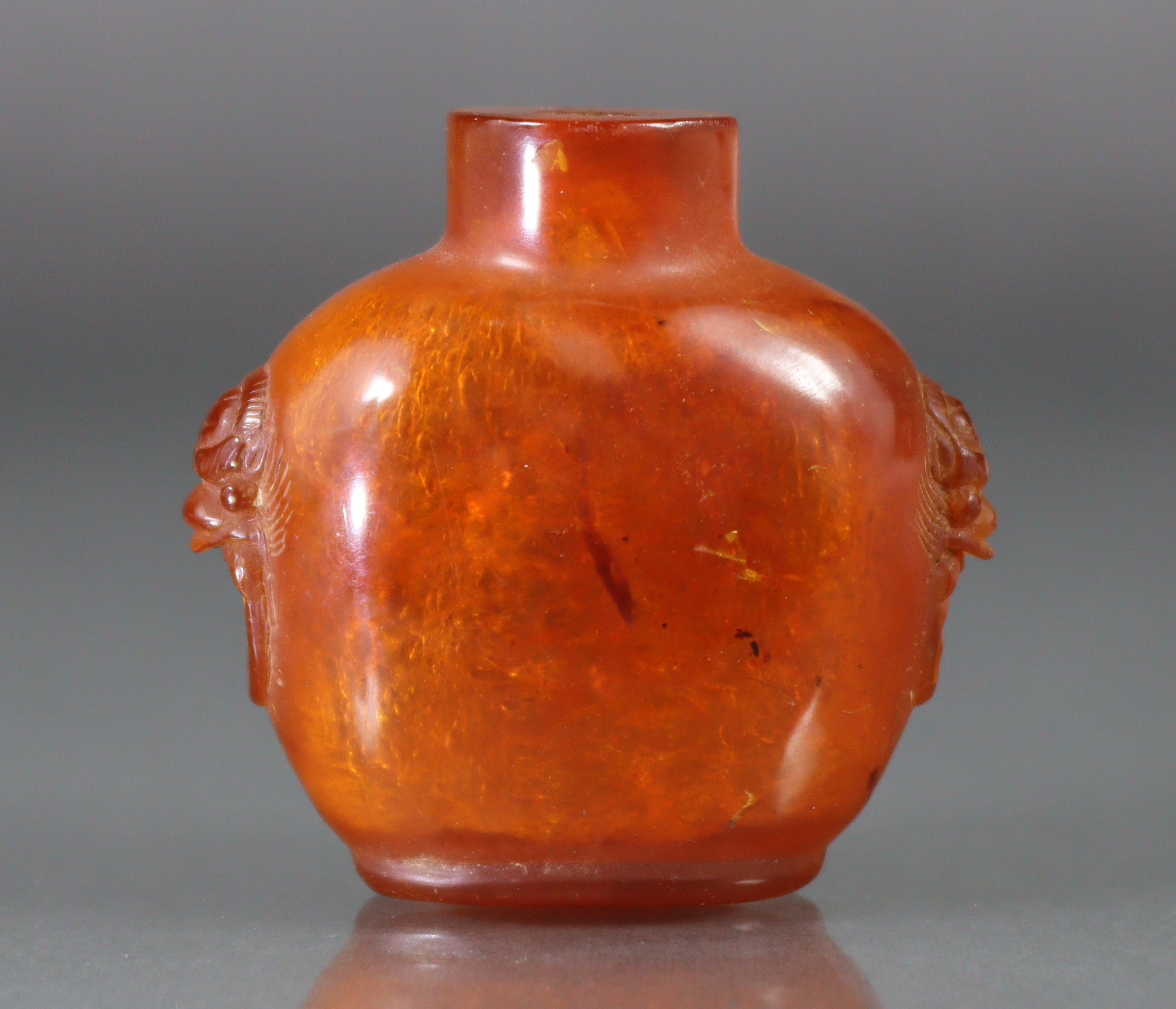 A Chinese carved golden amber snuff bottle of compressed form, with mask-&-ring handles to each