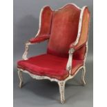 A 19th century French wing-back armchair in the Louis XV style with foliate carved painted frame,