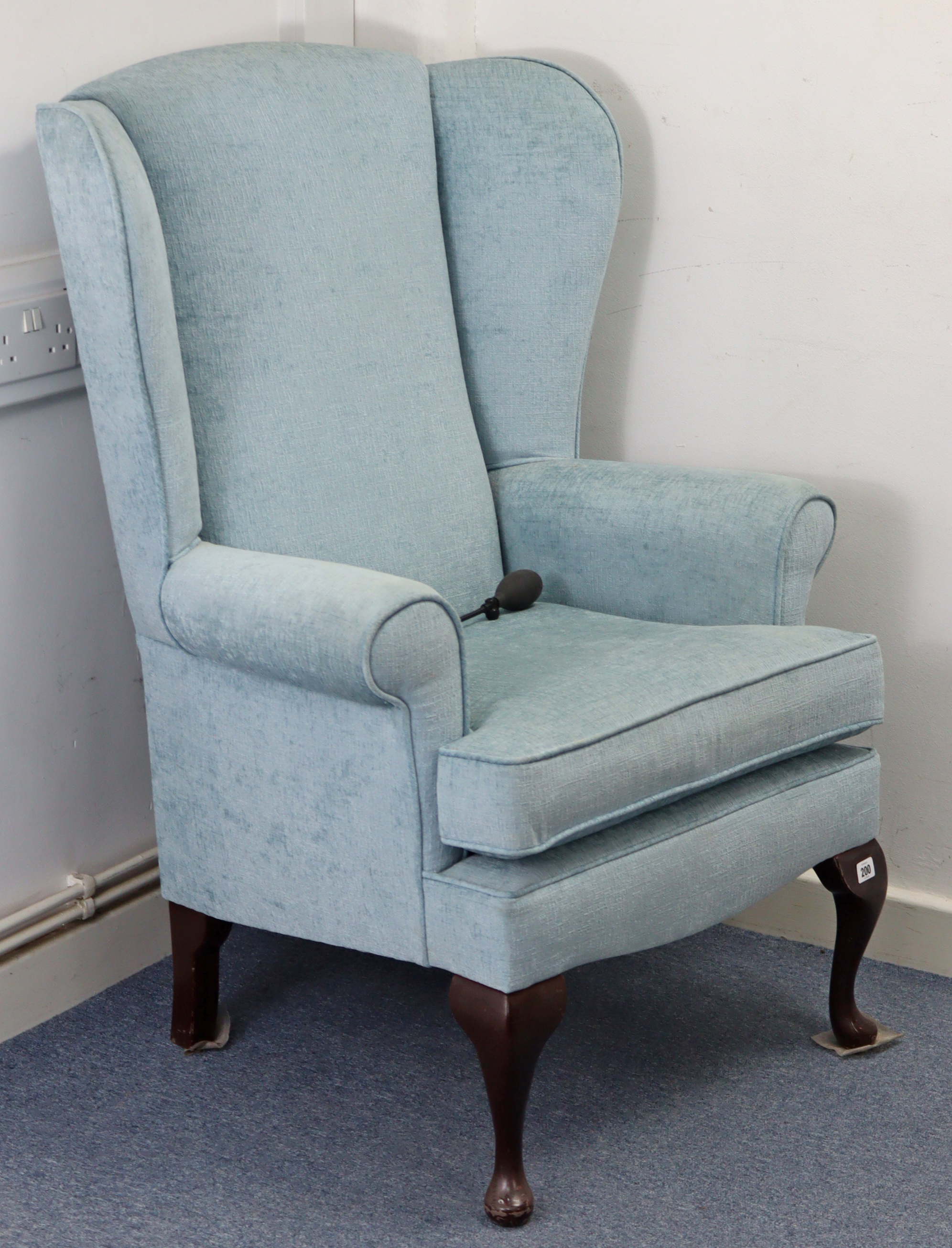 A wing-back armchair upholstered pale blue material, & on short cabriole legs.