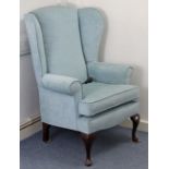 A wing-back armchair upholstered pale blue material, & on short cabriole legs.