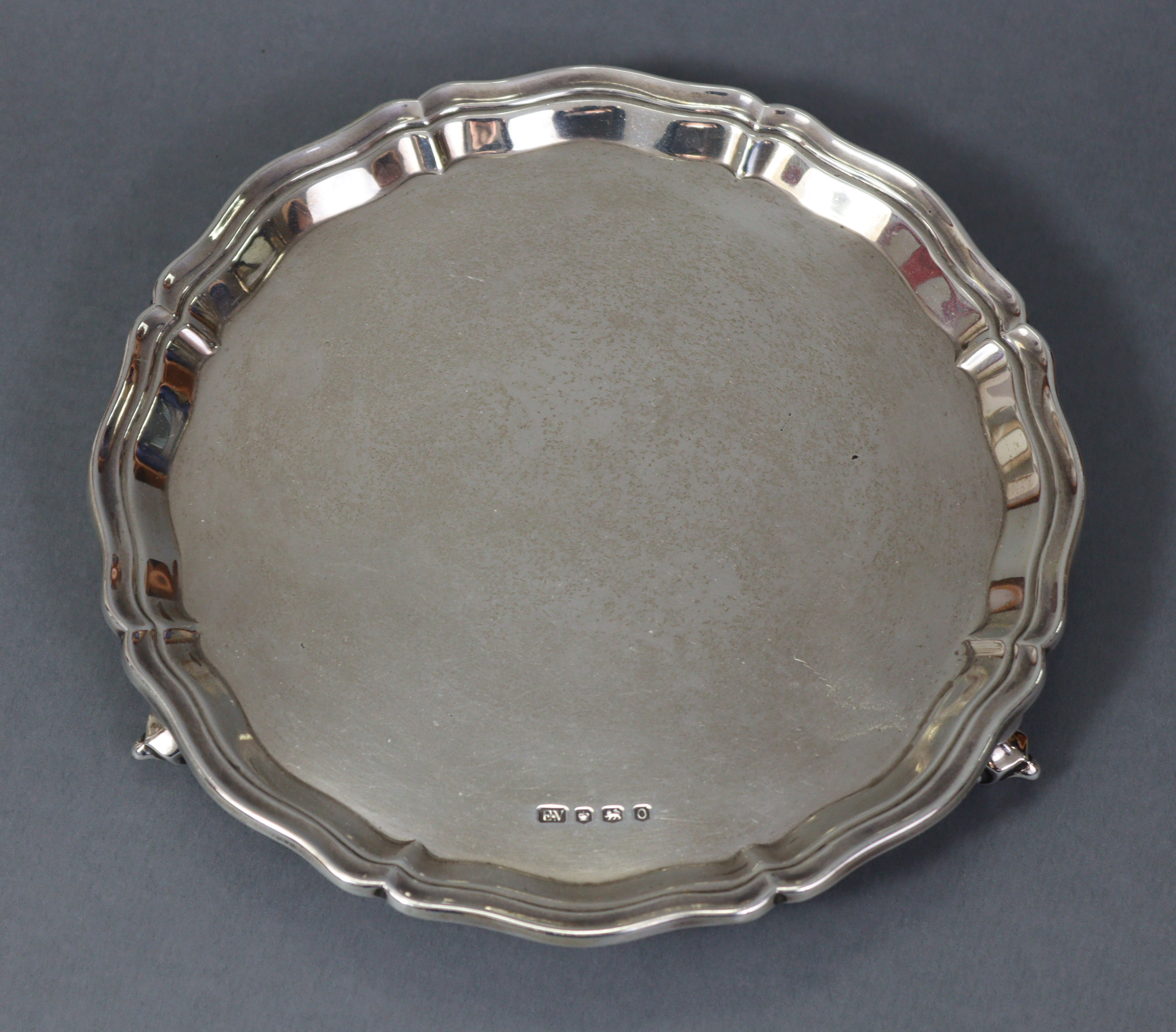 A George V silver waiter with raised pie-crust border, on three leaf-scroll feet, 8” diam.;