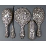 A silver-backed hand mirror & two hair brushes, each with embossed scroll decoration & engraved