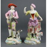 A pair of continental porcelain male & female standing costume figures in the Chelsea style, she