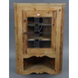 A pine hanging corner cabinet fitted two shaped shelves enclosed by a leaded stained glass door