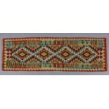 A Choli Kilim runner, with a multicoloured geometric pattern of four lozenges within a wide