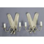 A pair or cream & gold painted metal wall sconces in the form of crossed feathers, each with twin