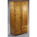 A pine twin-door wardrobe enclosed by pair of fielded doors above two small drawers, & on bun