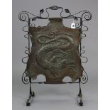 An Edwardian wrought-iron fire screen the copper plate with embossed dragon design, 23” wide x 31”