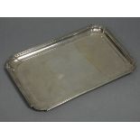 A George V silver rectangular dressing table tray with raised border, reeded rim, & rounded corners,