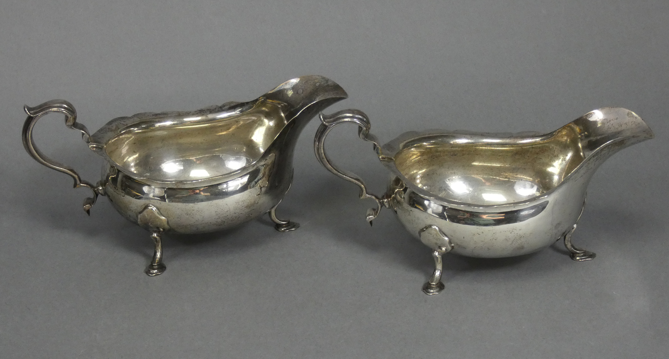 A pair of Georgian-style silver sauce boats with card-cut rims & scroll handles, each on three splay