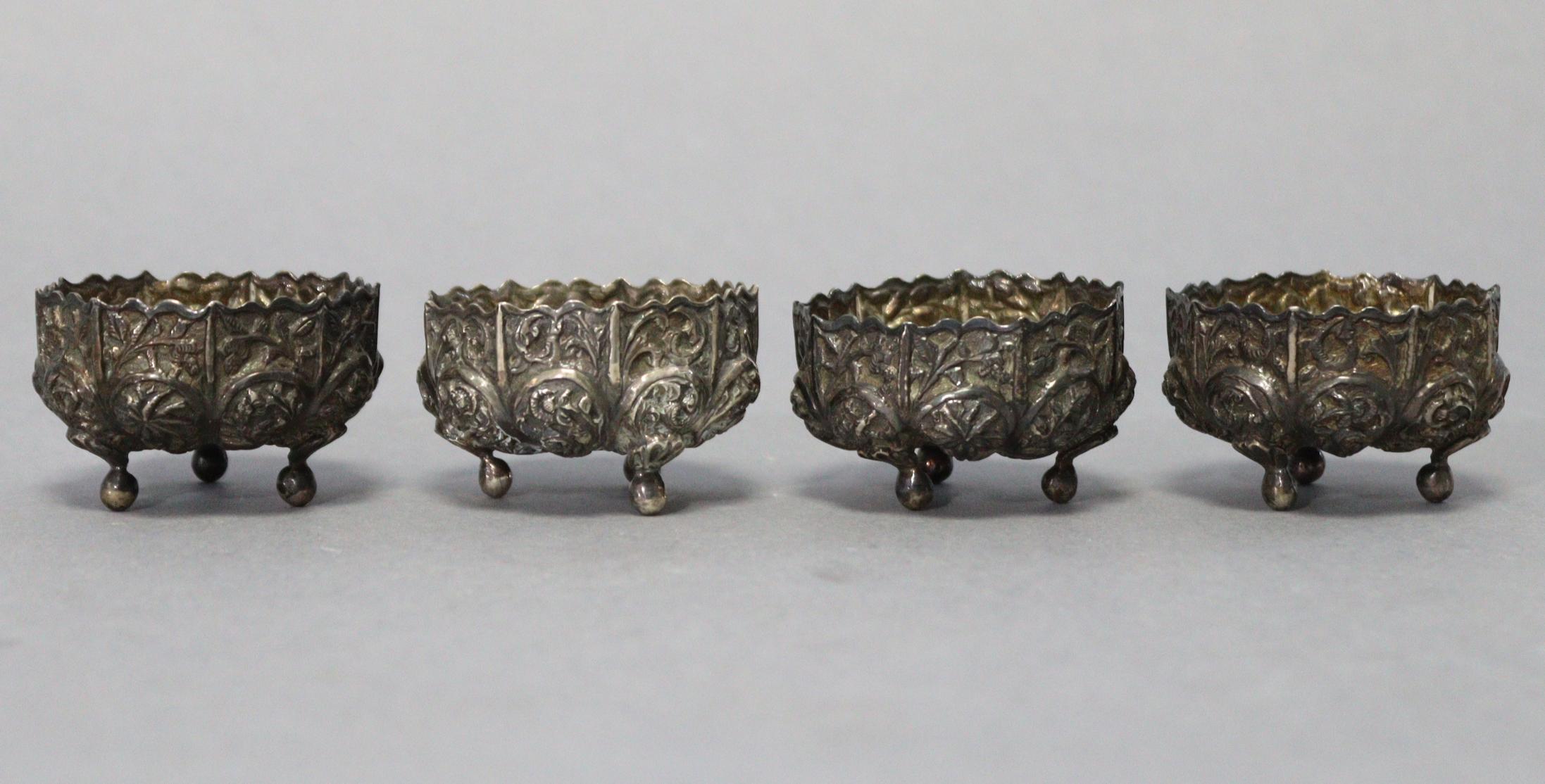 A set of four eastern white metal circular salt cellars with embossed scroll decoration, each on