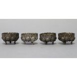 A set of four eastern white metal circular salt cellars with embossed scroll decoration, each on