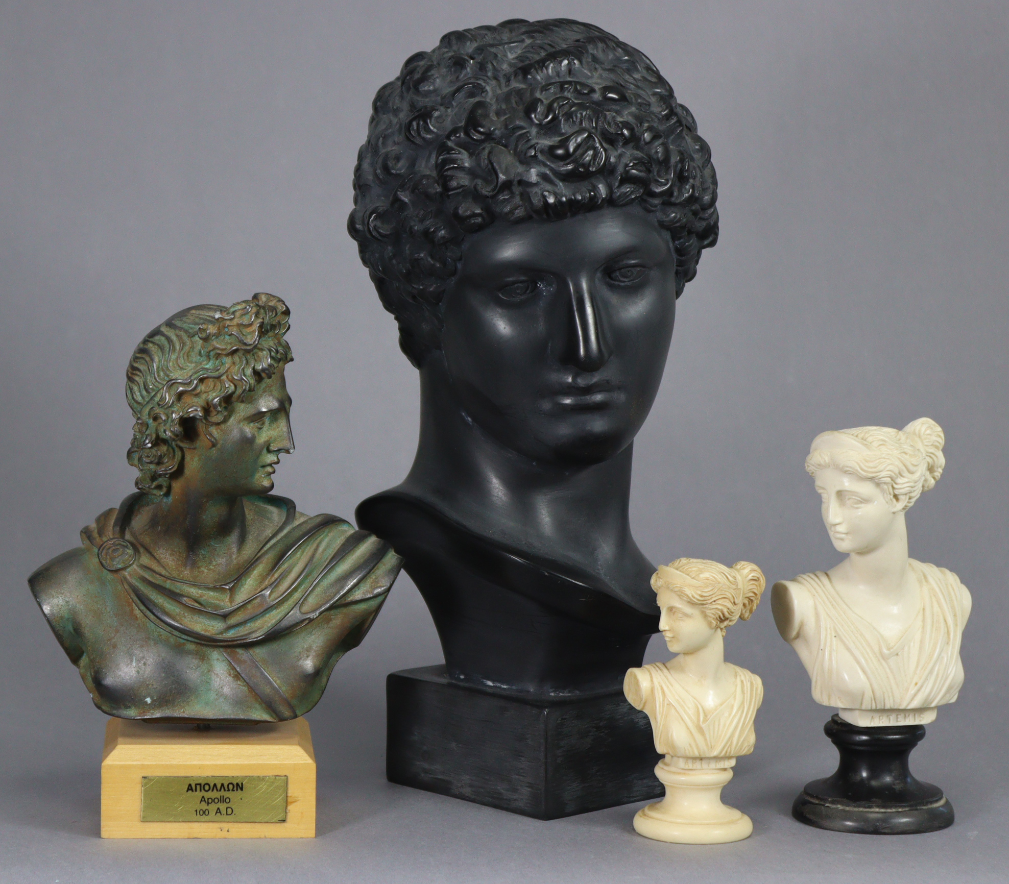 An ebonised resin bust of Antinous, on square base, 12” high; a bronzed composition bust of Apollo