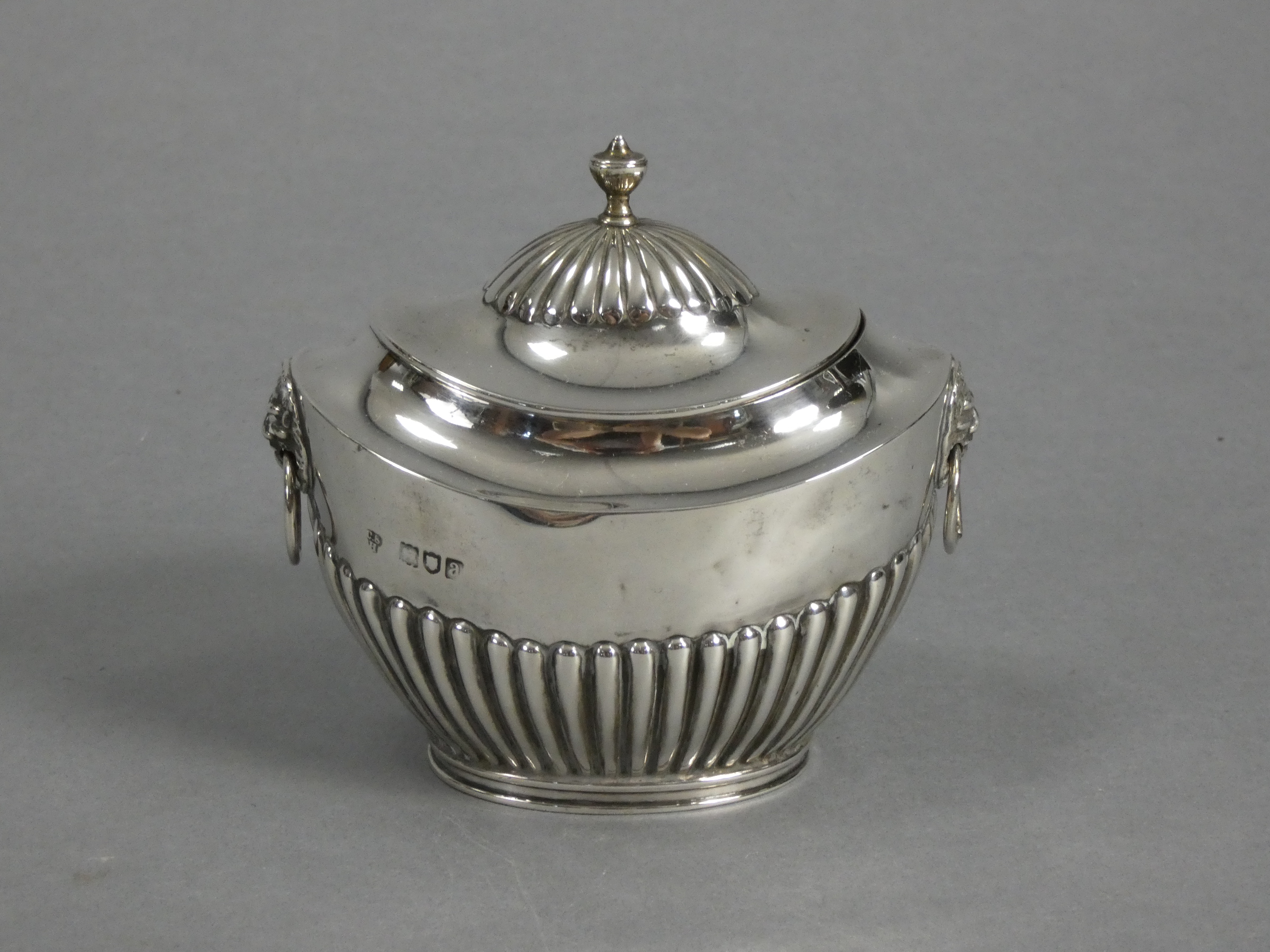 A late Victorian silver tea caddy of oval semi-fluted form, with hinged lid & lion-mask ring