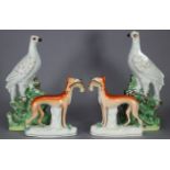 A pair of 19th century Staffordshire pottery models of Greyhounds, each holding a horse, 7½” wide