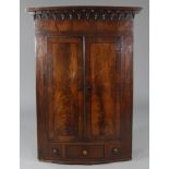 An early 19th century inlaid mahogany bow-front hanging corner cupboard, with moulded cornice