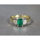 An emerald & diamond ring, the rectangular centre emerald weighting approx. 0.6 carat, flanked by