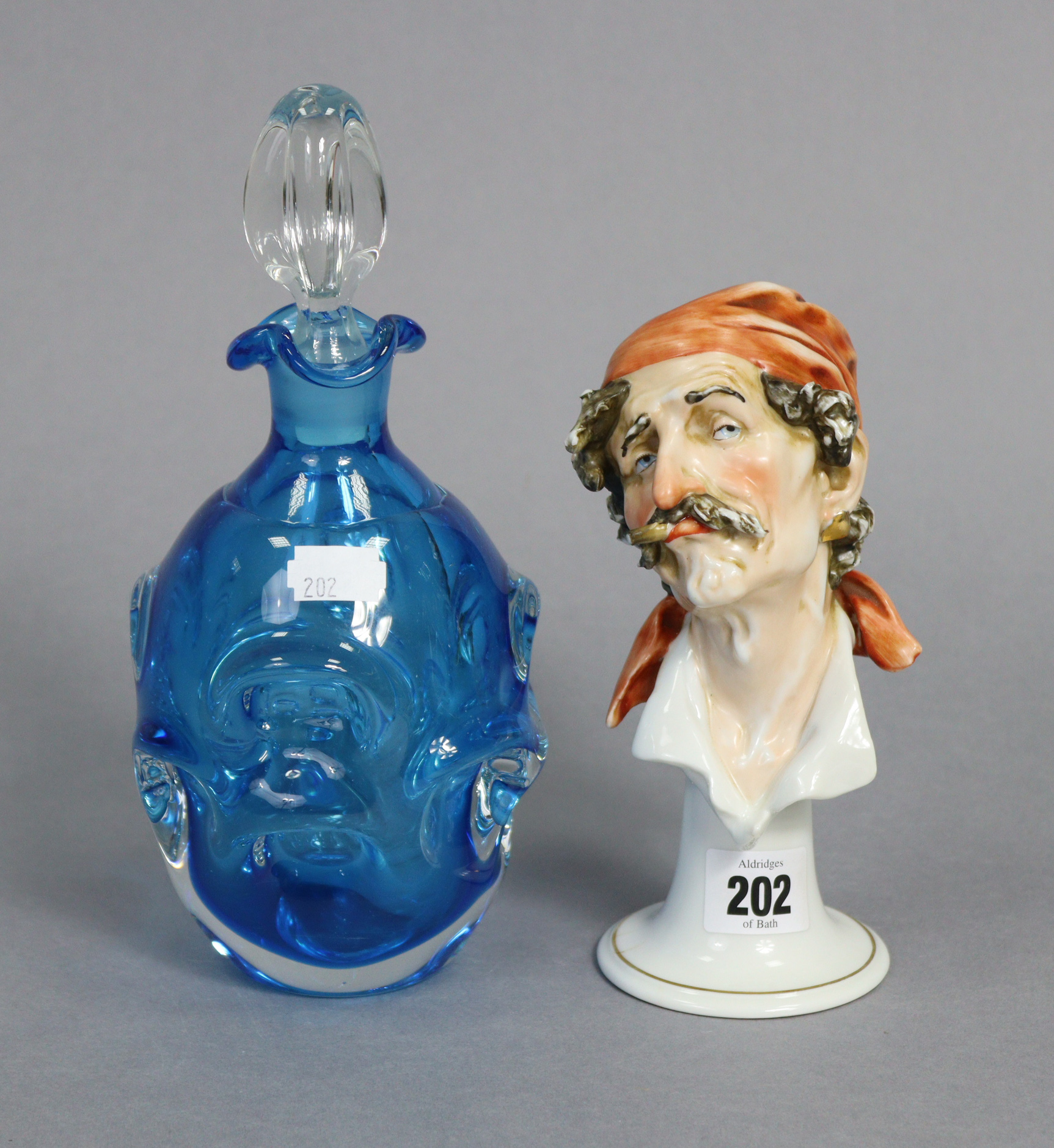 A continental porcelain ornament in the form of a male bust wearing a headscarf & puffing on a