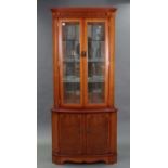A reproduction yew wood tall standing bow-front corner display cabinet fitted three plate-glass