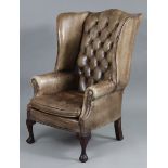 A wing-back armchair upholstered brass-studded tan leather, on wooden cabriole legs.