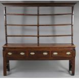 A George III elm dresser, with open shelves above three frieze drawers with brass oval handles, on