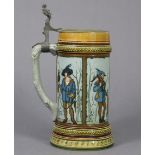 A Mettlach stoneware tankard with coloured & incised decoration of hunters, & hinged metal cover,