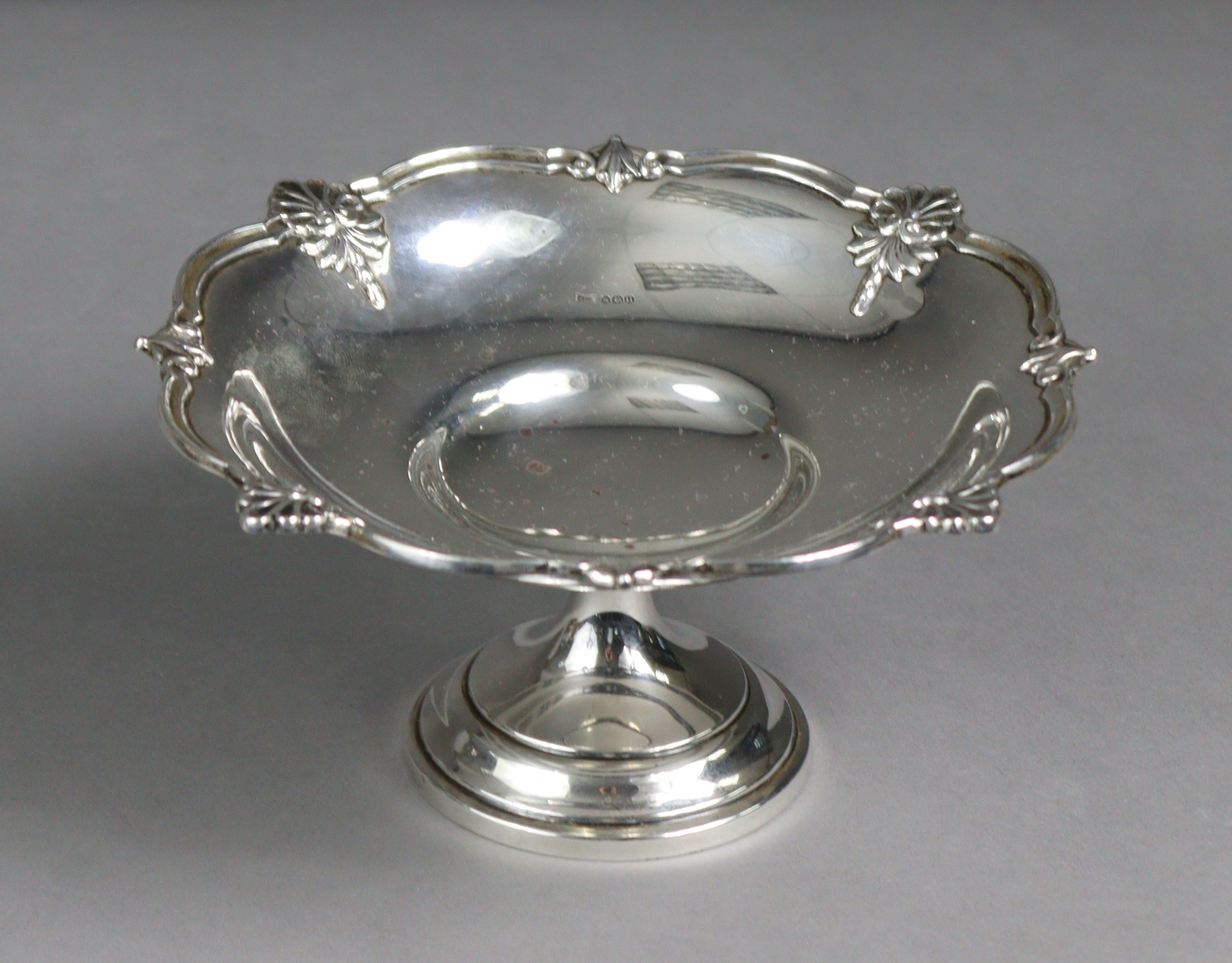 A silver circular sweetmeat dish with embossed shell & swag decoration to the shaped rim, on