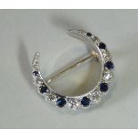 A diamond & sapphire crescent brooch set alternating graduated stones to un-marked yellow & white