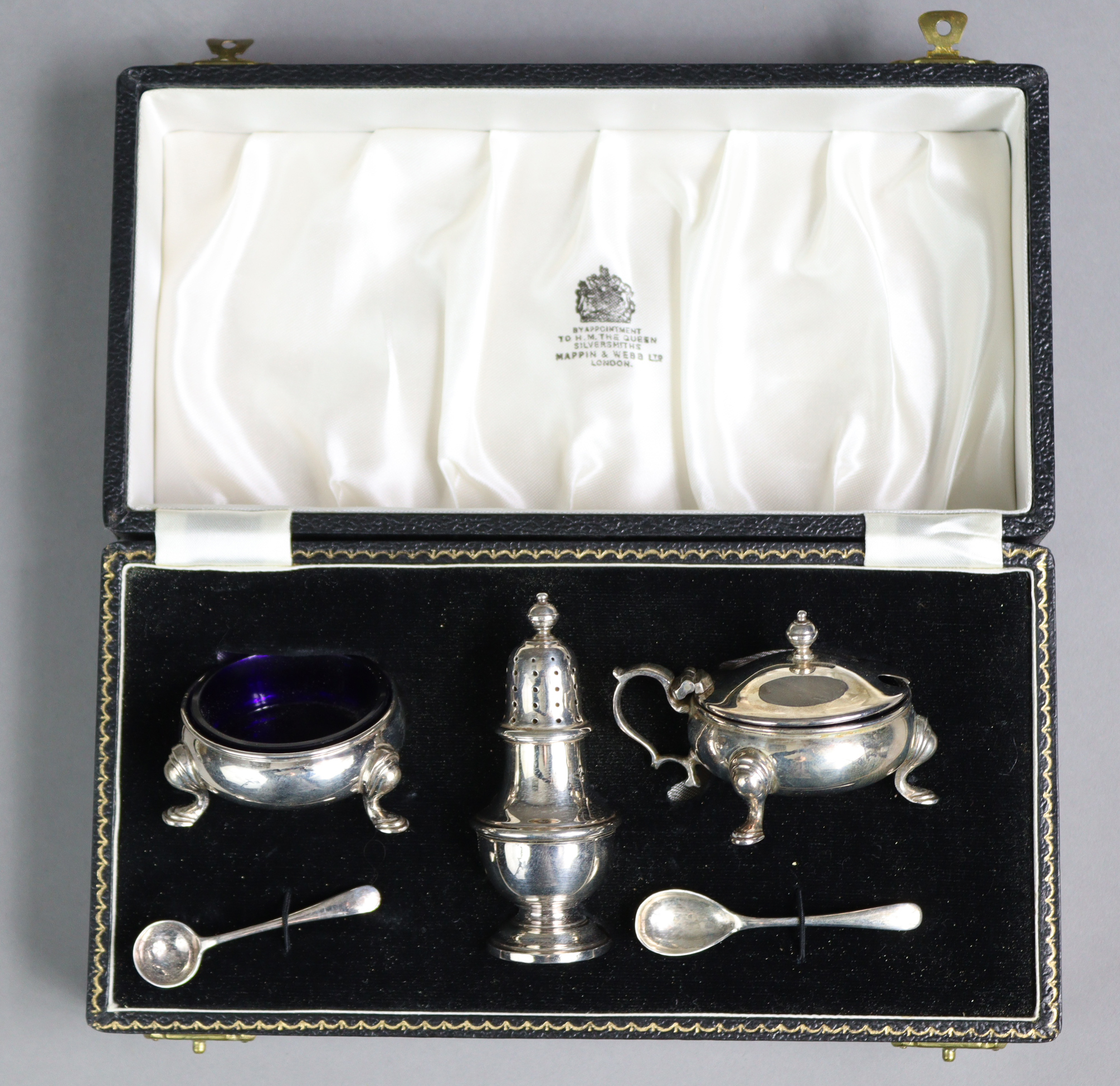 A silver three-piece condiment set comprising two squat round salts with blue glass liners & a