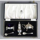 A silver three-piece condiment set comprising two squat round salts with blue glass liners & a