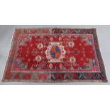 A Persian rug of crimson ground with central lozenge motif surrounded by multicoloured geometric