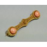 A yellow-metal ‘dumb-bell’ shaped bar brooch with canetile decoration, set coral cabochon either