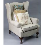 A Georgian-style wing-back armchair upholstered fawn material, & on short cabriole legs & pad feet.