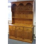 A pine dresser the upper part fitted two open shelves & with panelled back, the base fitted three