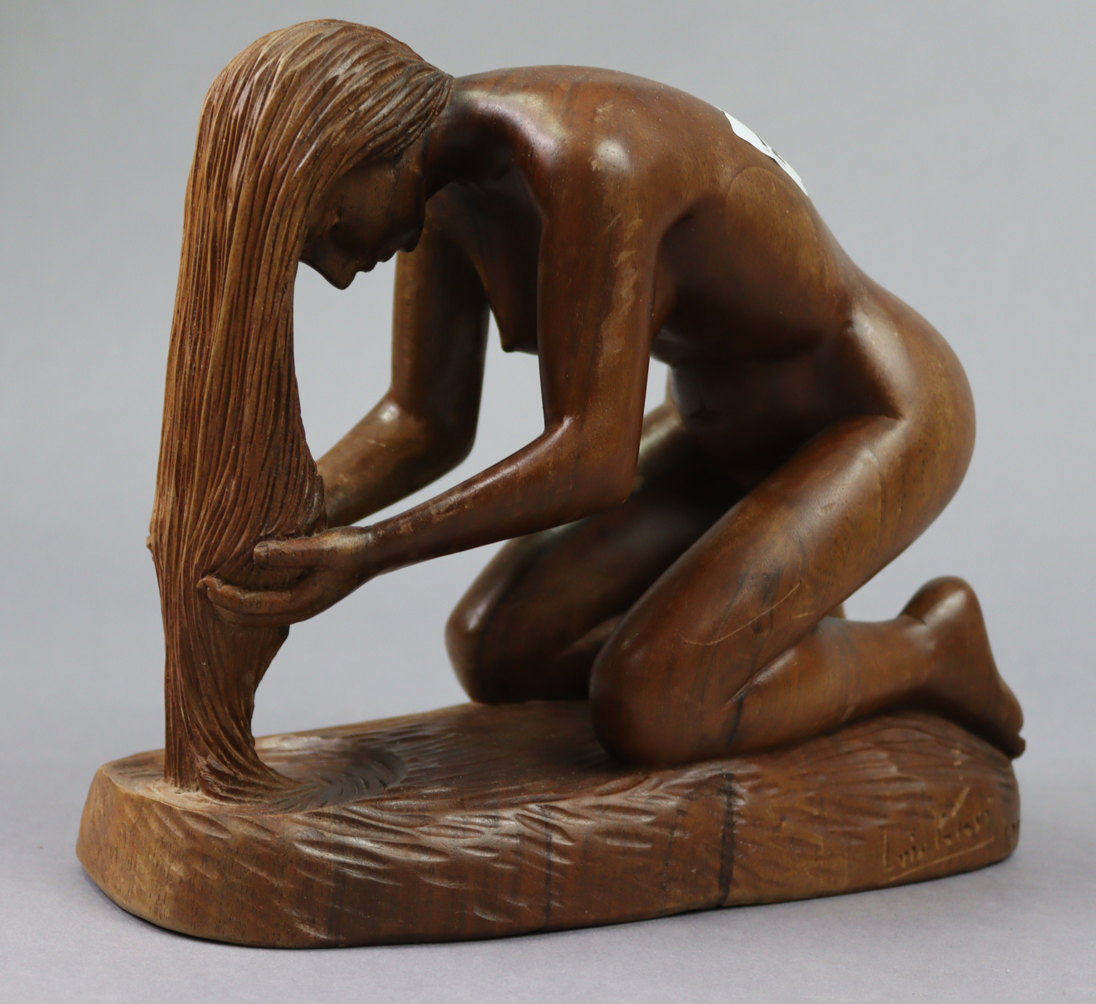 A carved wooden ornament in the form of a kneeling female figure holding her hair in her hands