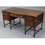 A 1930’s oak knee-hole desk fitted with an arrangement of five drawers, & on baluster-turned