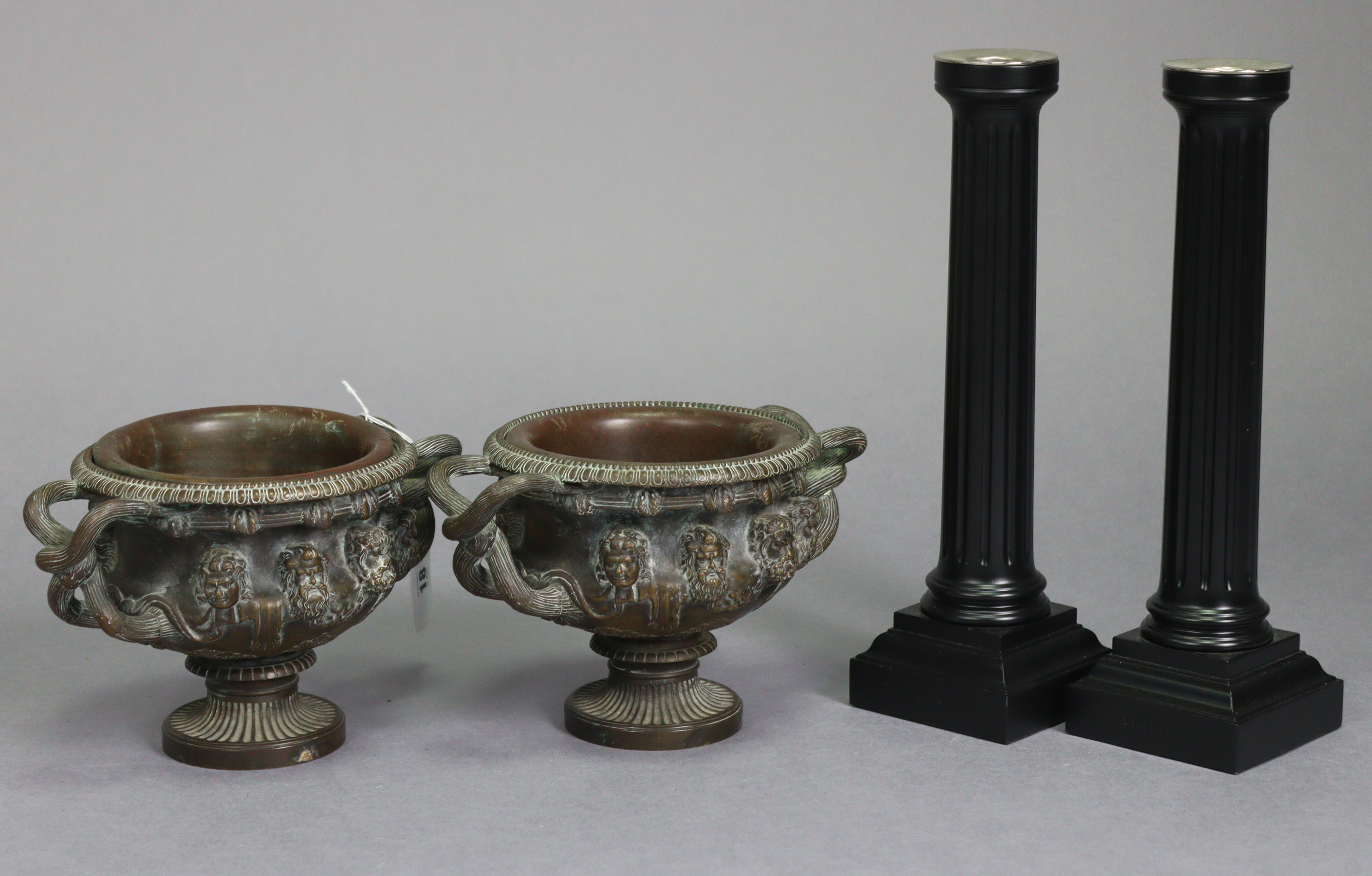 A pair of bronzed circular two-handled vases each with raised mask design & on a round pedestal